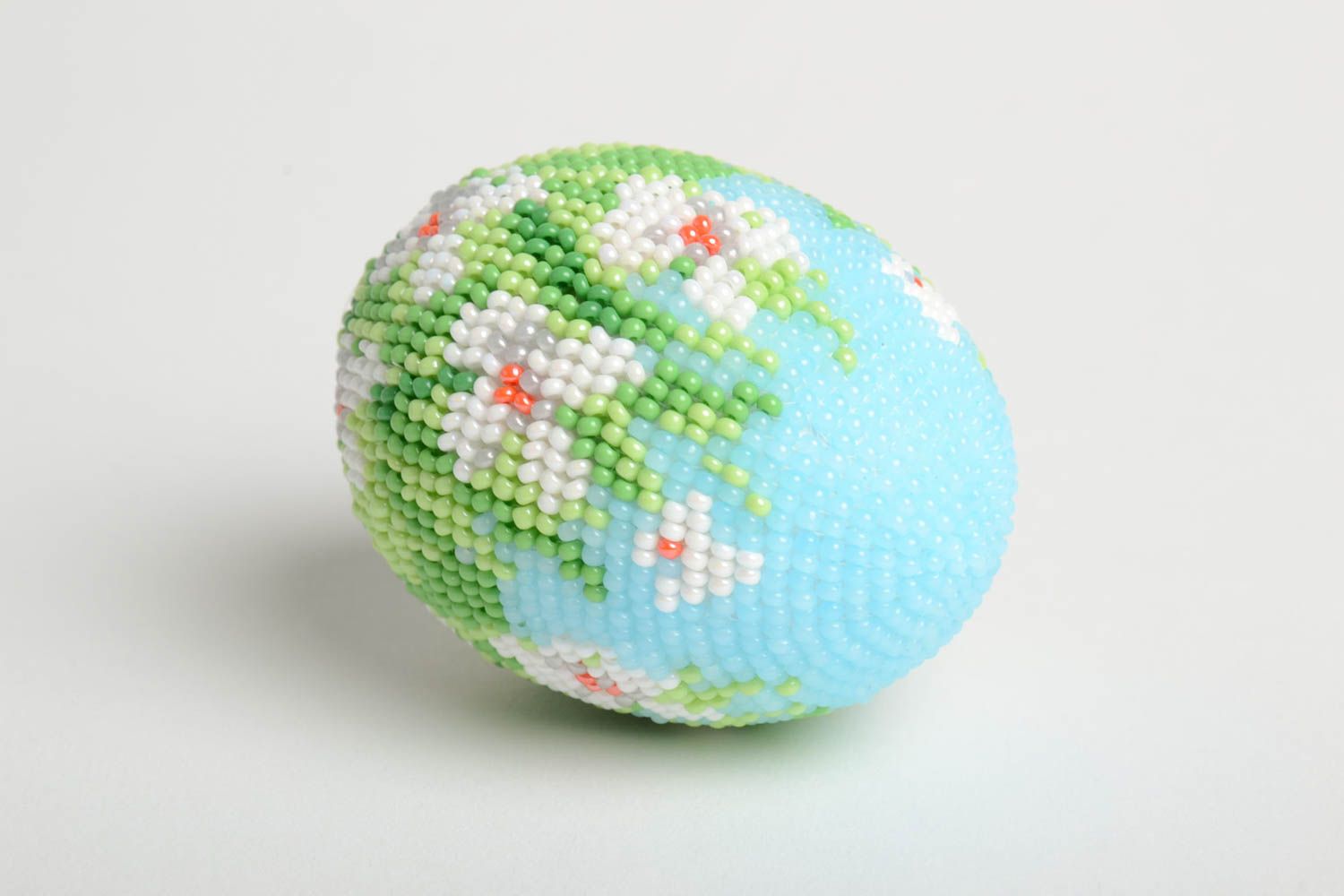 Statuette - beaded egg, with the image of white flowers in a green meadow.